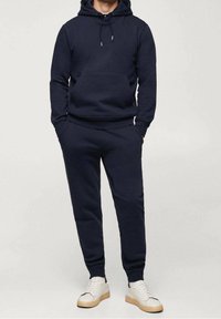 Completo felpa blu navy composto da hoodie e pantaloni della tuta in tessuto morbido. La hoodie presenta una tasca frontale e un cordino regolabile; i pantaloni hanno polsini elasticizzati.