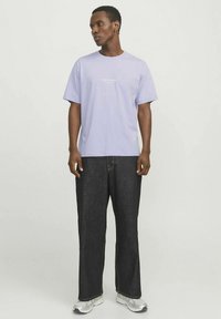 Šviesiai violetinė trumpomis rankovėmis su apvalia iškirpte ir baltais užrašais. Derinama su tamsiais džinsais ir sidabriniais sportbačiais. Lygaus audinio tekstūra.