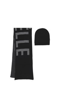 Scaldino in maglia nera con grandi lettere grigie e berretto abbinato in maglia nera posizionati uno accanto all'altro su sfondo bianco.