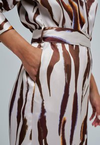 Blusa de satén con patrón marrón y blanco, con una cintura entallada y bolsillo lateral, que presenta rayas similares a pinceladas en diferentes tonalidades.