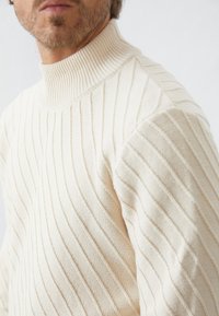 Man som bär en off-white ribbade polotröja med diagonala stickade mönster och texturerade detaljer.