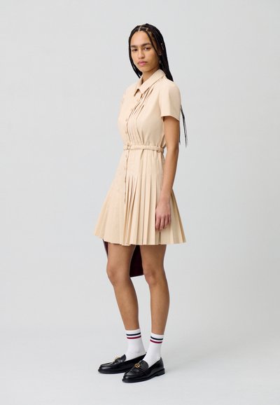Vestido de manga corta, beige, con pliegues y cinturilla ajustada. Combinado con mocasines negros y calcetines blancos con rayas rojas y azules.