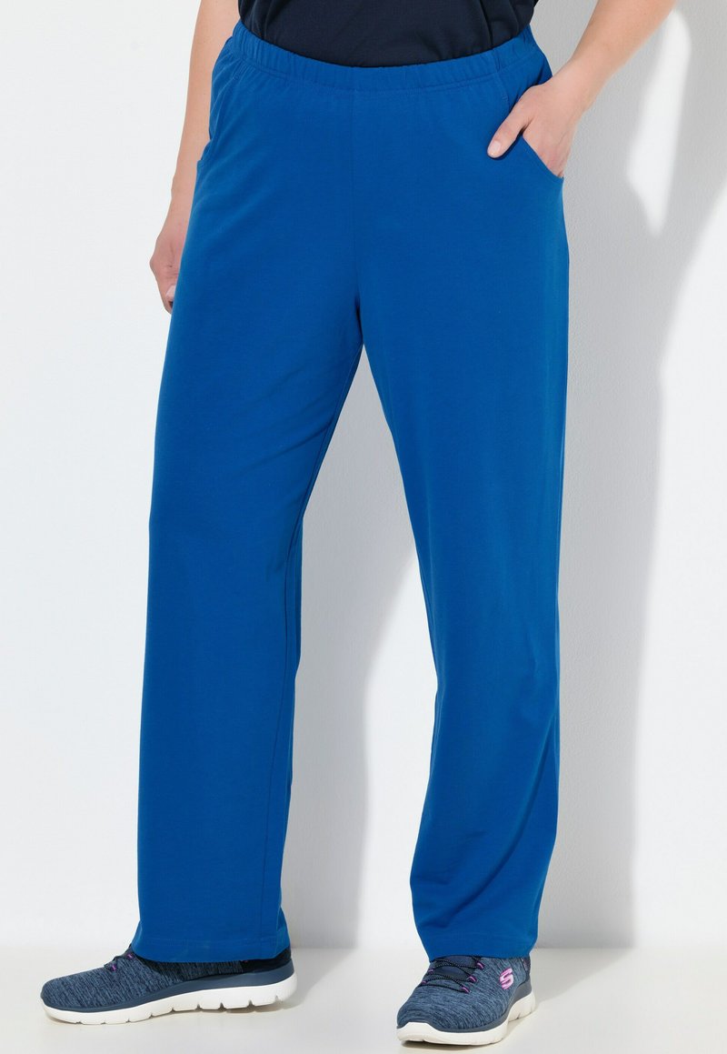 Blå, stretchiga byxor i tyg med elastisk midja, sidofickor och en avslappnad passform, kombinerade med mörka mönstrade träningsskor.