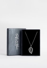 Silvrig bladformad halsband med en delikat kedja, med klara utsmyckningar längs bladets kant, presenterat i en svart sammetfodrad låda.