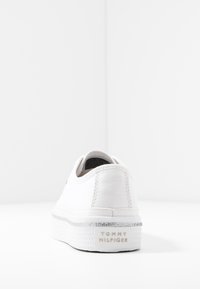 Bílé tenisky Tommy Hilfiger z pohledu zezadu, s tlustou podrážkou a stříbrným třpytivým pruhem a logem značky na patě.