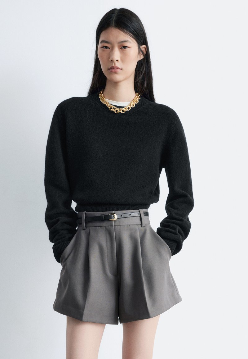 Sort strikket sweater med høj hals, kombineret med grå, højtaljede og skræddersyede shorts. Tilbehør med en chunky guldkæde halskæde.