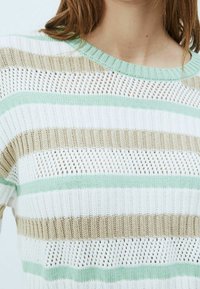 Strikket sweater i hvid, grøn og beige striber. Har et struktureret, åbent vævemønster med en ribbet krave og korte ærmer.