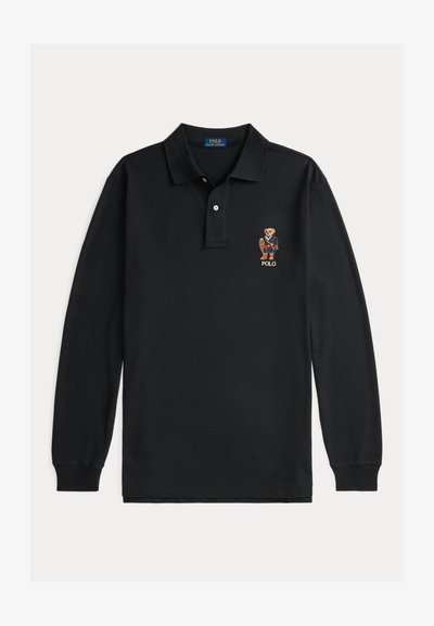 Juodame ilgomis rankovėmis polo marškiniai su apykakle, dviem priekiniais mygtukais ir siuvinėtu lokiu, dėvinčiu švarką ir batus, virš "POLO" teksto ant krūtinės.