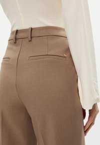 Καφέ ραμμένα παντελόνια με υφή, με δύο πίσω τσέπες και ένα χρυσό κουμπί κοντά στη μέση.