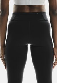 Leggings neri a vita alta con una superficie liscia, dotati di una tasca con zip discreta sulla vita e senza cuciture visibili.