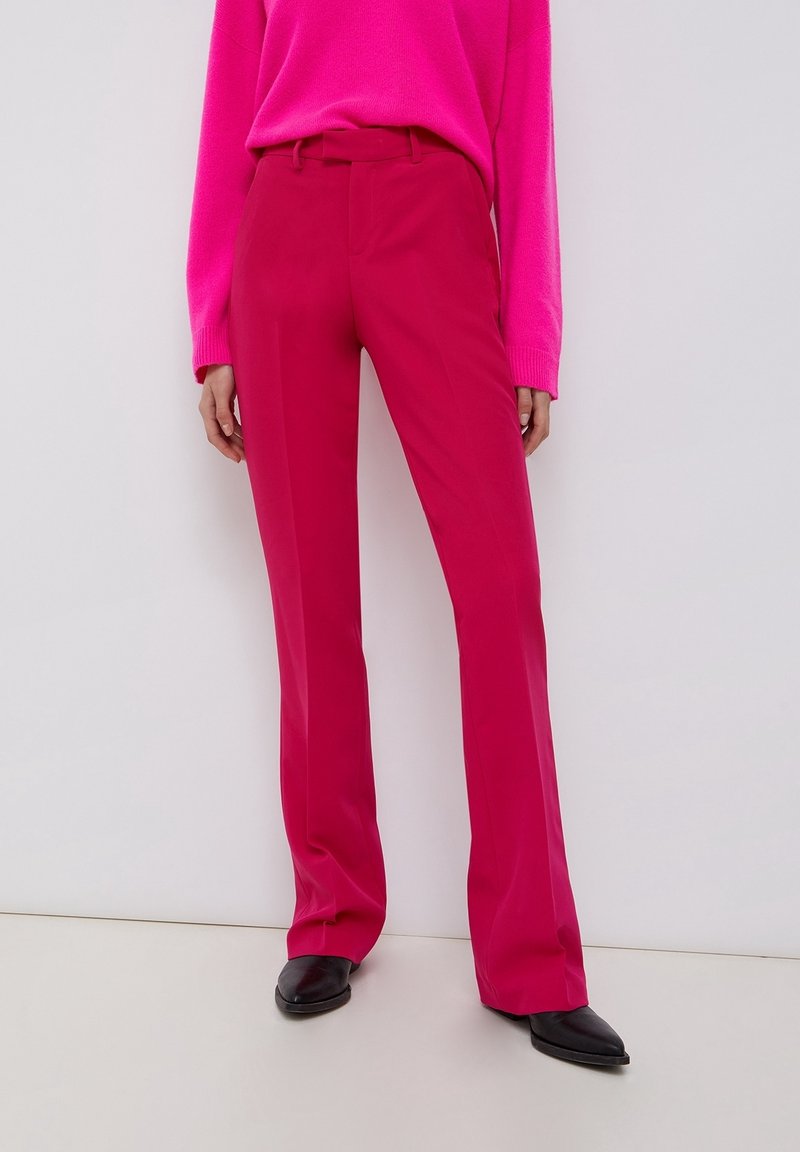 Slim fit, výrazné růžové, vysoké kalhoty s hladkou strukturou. Vytvořeno v kombinaci s odpovídajícím svetrem s dlouhými rukávy a černými podpatky.
