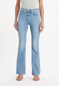 Les jeans évasés bleu clair présentent une taille haute, un style à cinq poches et un léger effet délavé. Le matériau est en denim, avec une texture lisse.