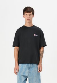 Zwarte katoenen t-shirt met oversized pasvorm, korte mouwen, ronde hals, met een kleurraf "Paradiso Airlines" graphic op de borst.