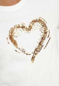 Camiseta blanca de algodón con un diseño de corazón en lentejuelas doradas y bronce, con una textura suave y escote redondo.