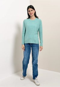 Jasnoniebieski sweter z dzianiny z okrągłym dekoltem, długimi rękawami, w połączeniu z prostymi niebieskimi dżinsami i białymi sneakersami.