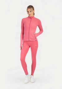 Pink athletic jacket with full zipper and fitted design, paired with matching leggings. Textured fabric, smooth finish, and minimal branding.