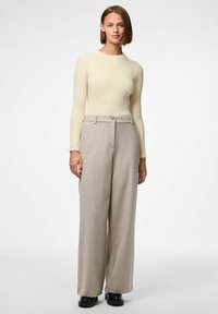Crème geribbelde long-sleeve top in combinatie met lichtbeige wijdvallende broeken met knoopsluiting en klassieke zakken, allemaal in zachte stof.