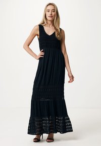 Svart maxiklänning med V-ringning, smockad midja, textil med struktur och spetskant vid nederkanten. Designad med åtsittande överdel och lager-på-lager kjol.