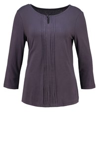 Ciemnofioletowa bluzka z długim rękawem o okrągłym dekolcie, z pionowymi fałdami z przodu i małym ozdobnym guzikiem na górze.