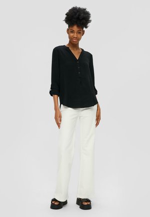 Chemise noire à manches longues avec un col en V et des détails de boutons, associée à un pantalon blanc évasé et des chaussures à talons épais noires. Tissu texturé.