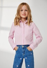 Skraćena ružičasto-bijela prugasta košulja s ovratnikom i jednim džepom na prsima, u kombinaciji s trapericama visokog struka u plavoj boji s uzorkom ružičastih srca.