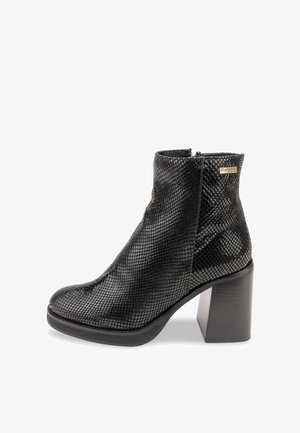 Botín negro hasta el tobillo con un acabado texturizado similar a la piel de serpiente, un tacón grueso y un cierre de cremallera en el lateral. Punta lisa y silueta elegante.