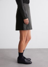 Sort læder mini nederdel med en glat tekstur, høj talje og A-line silhuet, parret med sorte loafers og sokker.