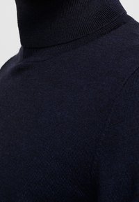 Pull col roulé bleu marine en maille fine avec une texture lisse. Il présente un col ajusté et une conception d'épaule sans couture.