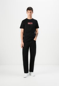 Zwarte katoenen t-shirt met een kleurrijke grafische print. Gecombineerd met zwarte broek en witte sneakers. Eenvoudig, rechtvallend ontwerp.