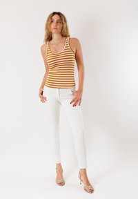 Top a righe arancione e crema, design aderente, abbinato a jeans skinny bianchi. Accentuato da tacchi beige con cinturini. Texture liscia.