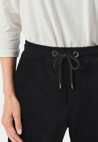 Zwarte corduroy joggers met een trekkoord tailleband met zilveren ringetjes, gestructureerde stof en een relaxte pasvorm, gecombineerd met een witte longsleeve.