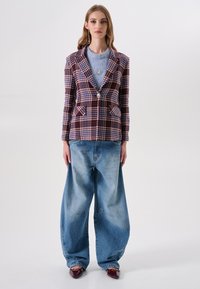 Ruitenblazer met tinten van lavendel, bordeauxrood en crèmekleur, met een enkele knoop en twee voorzakken, gecombineerd met losse blauwe spijkerbroeken.