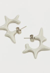 Σκουλαρίκια από λευκή ρητίνη σε σχήμα αστέρι, με γυαλιστερό φινίρισμα και ασημένιες μεταλλικές πίσω πλευρές για σταθερό κράτημα. Το μέγεθος και το βάθος ενισχύουν το σχεδιασμό.