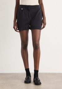 Pantalones cortos de algodón negro con corte recto, que presentan un bolsillo delantero y un detalle de botón, puños con dobladillo y una textura suave.