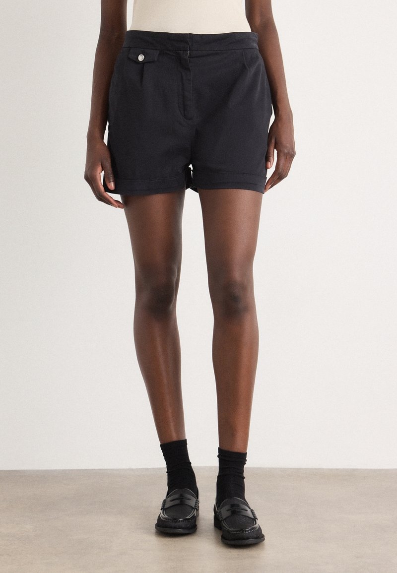 Pantalones cortos de algodón negro con corte recto, que presentan un bolsillo delantero y un detalle de botón, puños con dobladillo y una textura suave.