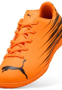 Helle orange Sportlichkeitsschuhe mit strukturiertem synthetischen Obermaterial, schwarzem Streifenmuster und schwarzem Puma-Logo. Verfügt über ein traditionelles Schnürsystem.