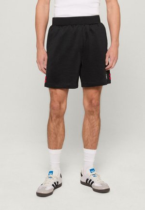 Zwarte sportshorts met een elastische taille, zijzakken en rode accentknopen op het linkerpijp. Gemaakt van zacht, gestructureerd materiaal.