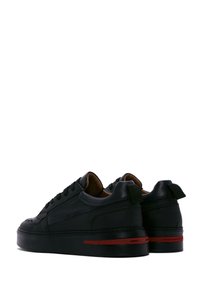 Baskets basses en cuir noir avec surface texturée, bout arrondi et bande rouge sur la semelle épaisse. Présentent un système de laçage et une languette d'enfilage.