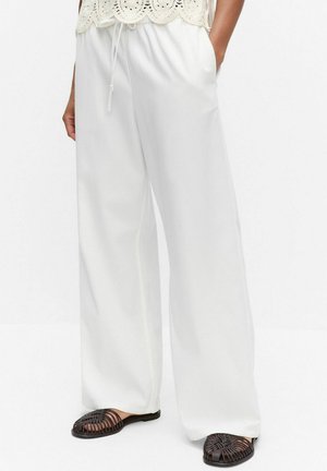 Valkoiset leveälahkeiset housut, joissa on nyörivyötärö, yhdistetty mustiin punottuihin slip-on-kenkiin ja kermaan vivahtavaan virkatun malliseen toppiin.