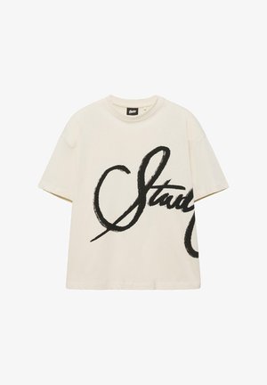 T-shirt à manches courtes de couleur crème avec un texte cursif noir surdimensionné sur le devant et un col rond.