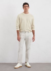 Light beige knit sweater with crew neck, paired with light gray trousers. Footwear is white sneakers with beige soles. Classic fit.