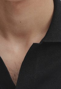 Sort poloshirt med krave, lavet af blødt stof. Viser et nærbillede af en ren halsudskæring med en glat tekstur og minimal syning.