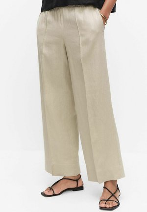 Beige linnen broek met wijd uitlopende pijpen en elastische taille, gedragen met zwarte sandalen met bandjes en een zwarte top.