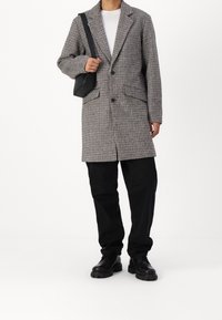 Abrigo de cuadros en blanco y negro, con solapa de muesca, dos botones y bolsillos delanteros. Combina con pantalones y zapatos negros.