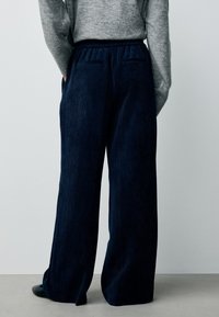 Pantaloni larghi in velluto a coste color blu navy con una texture a coste, dotati di una cintura elasticizzata e due tasche posteriori, indossati con un maglione grigio.