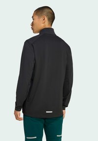 Black long-sleeve jacket featuring a textured fabric, high collar, and reflective accents. Back view shows the fit and design details.