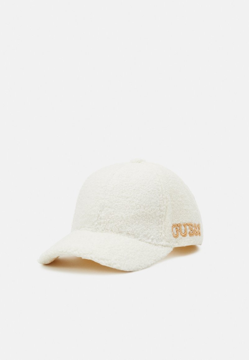 Casquette de baseball blanche texturée avec une visière courbée et un logo "GUESS" beige brodé sur le côté, présentée sur un fond uni.