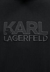 Μαύρο ύφασμα με ανάγλυφο κέντημα "KARL LAGERFELD", που περιλαμβάνει ένα προφίλ πλευρική σιλουέτα ενσωματωμένη στο γράμμα K.