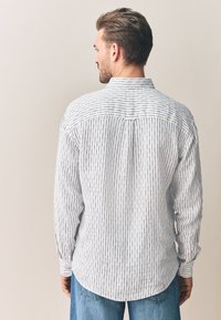 Herrenhemd mit Streifen aus leichtem Stoff, mit Knopfkragen und langen Ärmeln. Das Design zeigt dünne, vertikale marineblaue Streifen auf weißem Hintergrund.