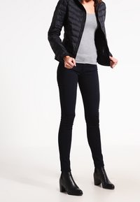 Black puffer jacket with a quilted design, gray fitted top, dark skinny jeans, and black heeled ankle boots. Smooth textures throughout.